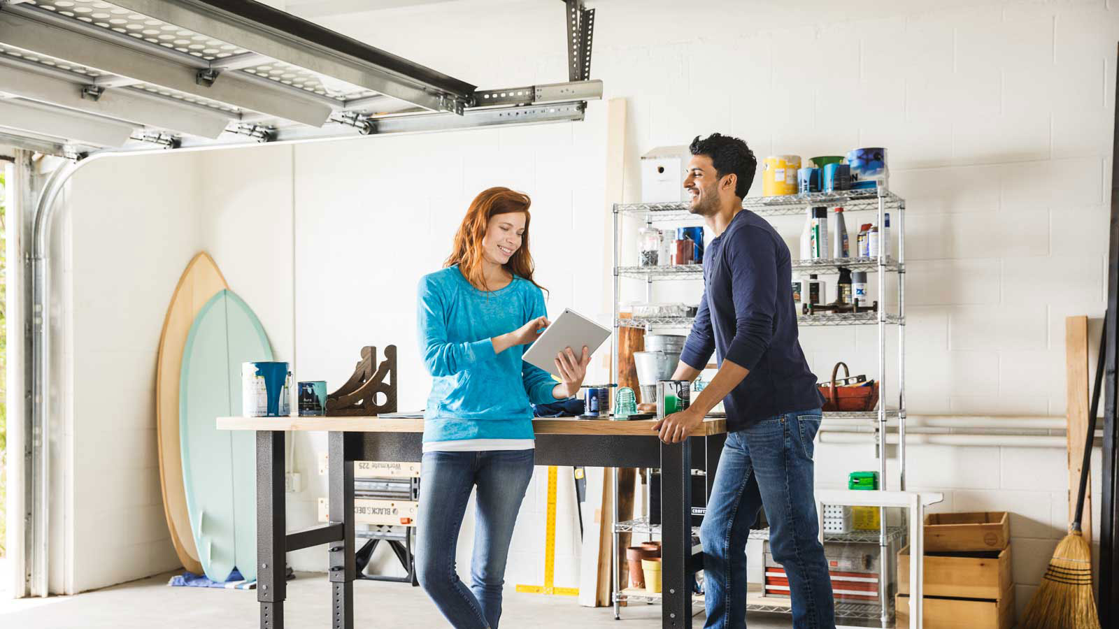 Visa - Pagos persona a persona Happy man and woman talking while standing in a home garage and looking at a tablet.