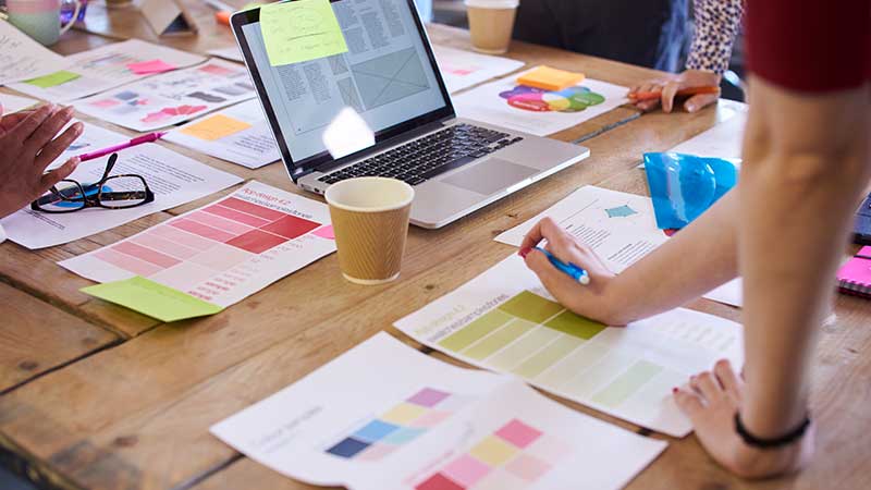 Mujer trabajando en equipo con diferentes gráficos sobre la mesa y una notebook